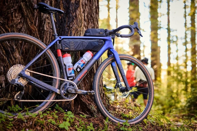 Blaues Gravel Bike mit Ausr&uuml;stung lehnt an einem Baum im Wald.