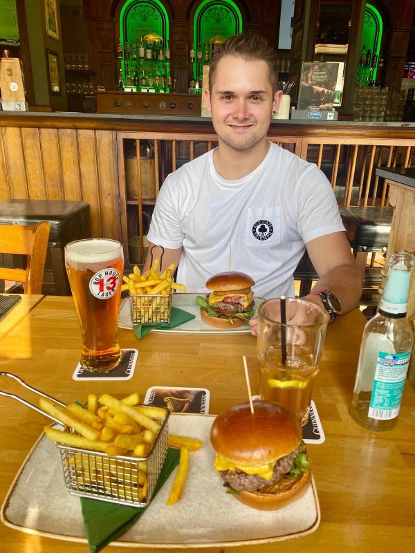 Ein Mann sitzt an einem Tisch in einem Restaurant und genie&szlig;t Burger, Pommes und Bier.