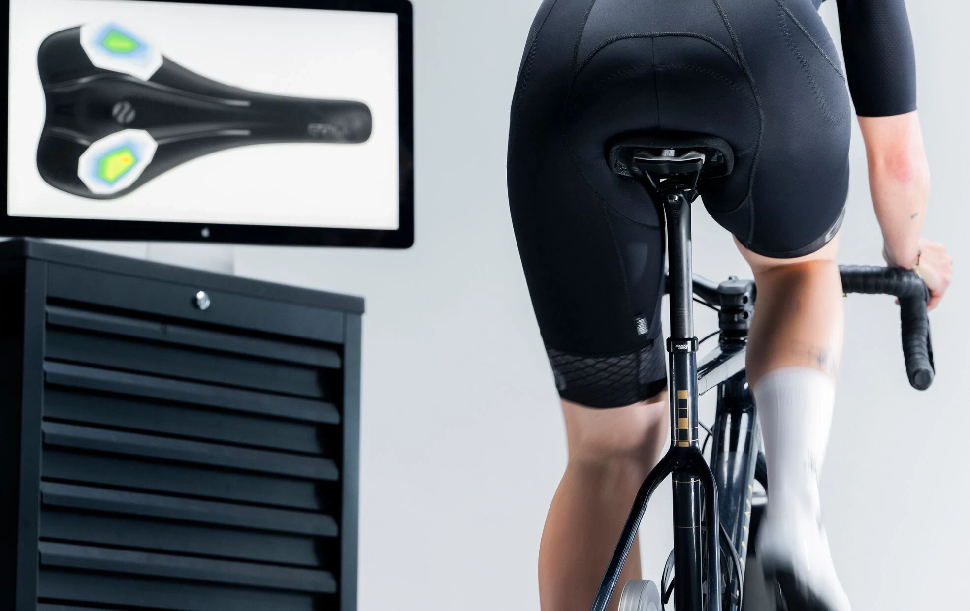 Fahrradfahrerin auf Sattel mit Druckverteilungs-Analyse auf Monitor.