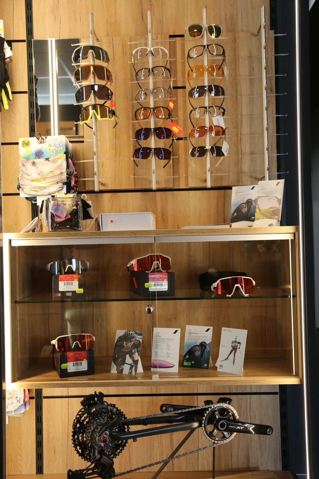 Ausstellungsfenster mit Sonnenbrillen an St&auml;ndern oben und Sportbrillen sowie Fahrradteile in Regalen unten.
