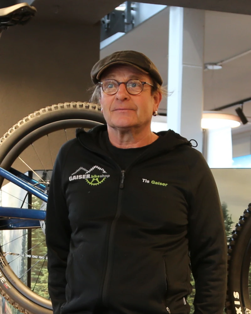 Mann mit Brille und Kappe im Gaiser-Bikeshop neben einem Fahrradreifen.